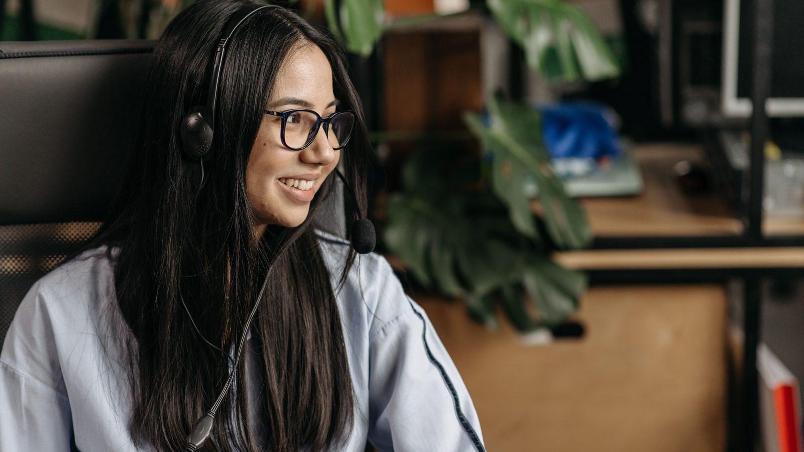 A friendly team member smiling during a phone conversation at a bright, plant-filled desk