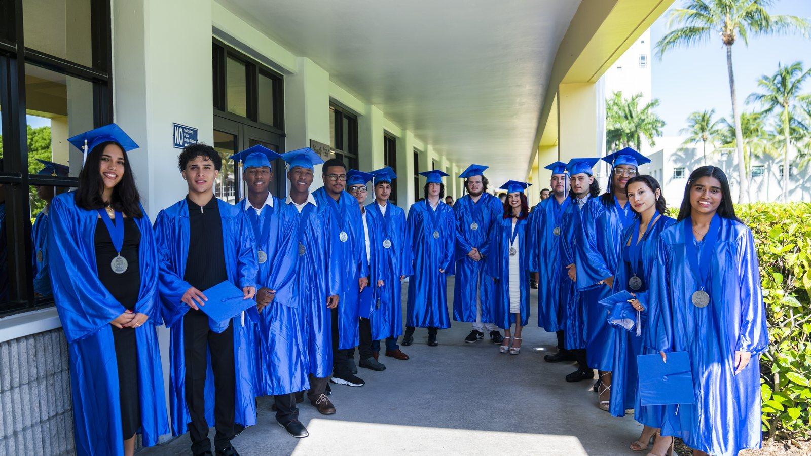 Graduates in blue caps and gowns with their medals, gathered outside on graduation day